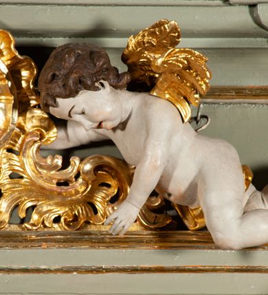 Zdjęcie nr 12: Ołtarz  jednoosiowy, jednokondygnacyjny ze zwieńczeniem. Podwójny cokół z wąską, drewnianą mensą ołtarzową, tabernakulum ze spływami wolutowymi. Retabulum flankowane dwiema ćwierć kolumnami skierowanymi po ukosie na zewnątrz, z których każda ujęta parą korynckich, kanelowanych pilastrów dźwigających przełamujące się nad nimi belkowanie i dwa faliste naczółki. Na tle pilastrów, na konsolach stoją dwa uskrzydlone anioły. Zwieńczenie ujęte spływami wolutowymi, zakończone profilowanym, lekko falistym gzymsem z dwiema stykającymi się wolutami. W polu głównym szeroka, złocona, prostokątna rama z obrazem "Św. Szymon Oracz", w zwieńczeniu owalny obraz w złoconej ramie z przedstawieniem św. Michała Archanioła. Figury aniołów wydrążone, ukazane w kontrapoście, o prawidłowych proporcjach ciała, w lekkim przechyleniu na bok, z dłońmi ułożonymi do gry na instrumencie szarpanym. Ich twarze są owalne o regularnych rysach, z brązowymi puklowanymi włosami sięgającymi ramion. Z tyłu przymocowane duże, złote skrzydła. Ubrani są w długie, złote szaty o ostrym zarysie. W partii belkowania para nagich puttów ze złoconymi opaskami na biodrach ujmują kartusz w rokokowym obramieniu. Na naczółkach z kolei siedzą nagie putta z przepaskami na biodrach i złotymi skrzydełkami. Na dekorację ornamentalną składają się drobne motywy roślinne, kampanule na ćwierćkolumnach, zwisy róż i gałązek wokół obrazu w zwieńczeniu i efektowna podwójna muszla palmetowa w zwieńczeniu. 



