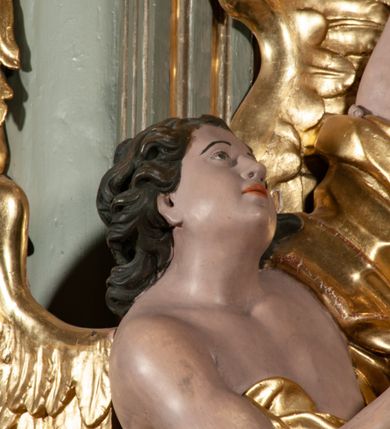 Zdjęcie nr 33: Ołtarz jednoosiowy, jednokondygnacyjny ze zwieńczeniem. Podwójny cokół z wąską, drewnianą mensą ołtarzową, wybrzuszoną. Na niej stoi tabernakulum ujęte narożnie ustawionymi spływami wolutowymi, zwieńczone spłaszczoną kopułką ze spływami wolutowymi. Retabulum flankowane dwiema ćwierć kolumnami skierowanymi po ukosie na zewnątrz, z których każda ujęta parą korynckich, kanelowanych pilastrów dźwigających przełamujące się nad nimi belkowanie i dwa faliste naczółki. Na tle pilastrów, na konsolach stoją figury św. Anny i św. Joachima oraz unoszą się na chmurach flankujące obraz uskrzydlone anioły. Zwieńczenie ujęte spływami wolutowymi, zakończone profilowanym, lekko falistym gzymsem z dwiema stykającymi się wolutami. N naczółkach dwa uskrzydlone, przepasane opaską na biodrach aniołki. W polu głównym szeroka, złocona, prostokątna rama z obrazem Matki Boskiej z Dzieciątkiem i koroną w partii belkowania, a w zwieńczeniu owalny obraz w złoconej ramie z przedstawieniem św. Józefa z Dzieciątkiem. Figury św. Anny i św. Joachima ukazane w lekkim kontrapoście, w długich, obficie fałdowanych szatach. Anna trzyma prawą rękę na piersi, w lewej przytrzymuje połę płaszcza, natomiast Joachim ręce składa w geście modlitwy. Anioły klęczą na chmurach, usytuowanych na różnych poziomach, ubrane są w miękko, ale drobno fałdowane szaty, odsłaniające ich ramiona i górną część klatki piersiowej i wskazujący na obraz. Na dekorację ornamentalną składają się drobne motywy roślinne, kampanule na ćwierćkolumnach, zwisy róż i gałązek palm wokół obrazu w zwieńczeniu i efektowna podwójna muszla palmetowa w zwieńczeniu. 