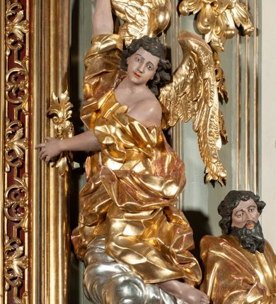 Zdjęcie nr 12: Ołtarz jednoosiowy, jednokondygnacyjny ze zwieńczeniem. Podwójny cokół z wąską, drewnianą mensą ołtarzową, wybrzuszoną. Na niej stoi tabernakulum ujęte narożnie ustawionymi spływami wolutowymi, zwieńczone spłaszczoną kopułką ze spływami wolutowymi. Retabulum flankowane dwiema ćwierć kolumnami skierowanymi po ukosie na zewnątrz, z których każda ujęta parą korynckich, kanelowanych pilastrów dźwigających przełamujące się nad nimi belkowanie i dwa faliste naczółki. Na tle pilastrów, na konsolach stoją figury św. Anny i św. Joachima oraz unoszą się na chmurach flankujące obraz uskrzydlone anioły. Zwieńczenie ujęte spływami wolutowymi, zakończone profilowanym, lekko falistym gzymsem z dwiema stykającymi się wolutami. N naczółkach dwa uskrzydlone, przepasane opaską na biodrach aniołki. W polu głównym szeroka, złocona, prostokątna rama z obrazem Matki Boskiej z Dzieciątkiem i koroną w partii belkowania, a w zwieńczeniu owalny obraz w złoconej ramie z przedstawieniem św. Józefa z Dzieciątkiem. Figury św. Anny i św. Joachima ukazane w lekkim kontrapoście, w długich, obficie fałdowanych szatach. Anna trzyma prawą rękę na piersi, w lewej przytrzymuje połę płaszcza, natomiast Joachim ręce składa w geście modlitwy. Anioły klęczą na chmurach, usytuowanych na różnych poziomach, ubrane są w miękko, ale drobno fałdowane szaty, odsłaniające ich ramiona i górną część klatki piersiowej i wskazujący na obraz. Na dekorację ornamentalną składają się drobne motywy roślinne, kampanule na ćwierćkolumnach, zwisy róż i gałązek palm wokół obrazu w zwieńczeniu i efektowna podwójna muszla palmetowa w zwieńczeniu. 