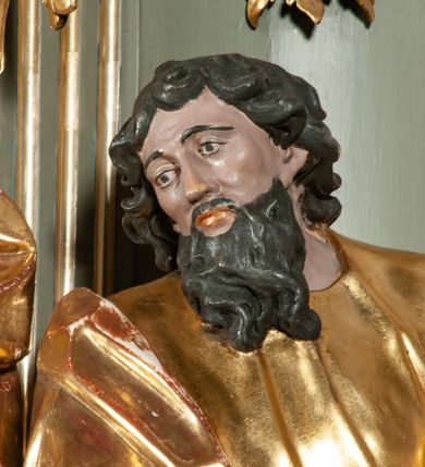 Zdjęcie nr 18: Ołtarz jednoosiowy, jednokondygnacyjny ze zwieńczeniem. Podwójny cokół z wąską, drewnianą mensą ołtarzową, wybrzuszoną. Na niej stoi tabernakulum ujęte narożnie ustawionymi spływami wolutowymi, zwieńczone spłaszczoną kopułką ze spływami wolutowymi. Retabulum flankowane dwiema ćwierć kolumnami skierowanymi po ukosie na zewnątrz, z których każda ujęta parą korynckich, kanelowanych pilastrów dźwigających przełamujące się nad nimi belkowanie i dwa faliste naczółki. Na tle pilastrów, na konsolach stoją figury św. Anny i św. Joachima oraz unoszą się na chmurach flankujące obraz uskrzydlone anioły. Zwieńczenie ujęte spływami wolutowymi, zakończone profilowanym, lekko falistym gzymsem z dwiema stykającymi się wolutami. N naczółkach dwa uskrzydlone, przepasane opaską na biodrach aniołki. W polu głównym szeroka, złocona, prostokątna rama z obrazem Matki Boskiej z Dzieciątkiem i koroną w partii belkowania, a w zwieńczeniu owalny obraz w złoconej ramie z przedstawieniem św. Józefa z Dzieciątkiem. Figury św. Anny i św. Joachima ukazane w lekkim kontrapoście, w długich, obficie fałdowanych szatach. Anna trzyma prawą rękę na piersi, w lewej przytrzymuje połę płaszcza, natomiast Joachim ręce składa w geście modlitwy. Anioły klęczą na chmurach, usytuowanych na różnych poziomach, ubrane są w miękko, ale drobno fałdowane szaty, odsłaniające ich ramiona i górną część klatki piersiowej i wskazujący na obraz. Na dekorację ornamentalną składają się drobne motywy roślinne, kampanule na ćwierćkolumnach, zwisy róż i gałązek palm wokół obrazu w zwieńczeniu i efektowna podwójna muszla palmetowa w zwieńczeniu. 