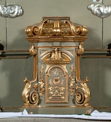 Zdjęcie nr 19: Ołtarz jednoosiowy, jednokondygnacyjny ze zwieńczeniem. Podwójny cokół z wąską, drewnianą mensą ołtarzową, wybrzuszoną. Na niej stoi tabernakulum ujęte narożnie ustawionymi spływami wolutowymi, zwieńczone spłaszczoną kopułką ze spływami wolutowymi. Retabulum flankowane dwiema ćwierć kolumnami skierowanymi po ukosie na zewnątrz, z których każda ujęta parą korynckich, kanelowanych pilastrów dźwigających przełamujące się nad nimi belkowanie i dwa faliste naczółki. Na tle pilastrów, na konsolach stoją figury św. Anny i św. Joachima oraz unoszą się na chmurach flankujące obraz uskrzydlone anioły. Zwieńczenie ujęte spływami wolutowymi, zakończone profilowanym, lekko falistym gzymsem z dwiema stykającymi się wolutami. N naczółkach dwa uskrzydlone, przepasane opaską na biodrach aniołki. W polu głównym szeroka, złocona, prostokątna rama z obrazem Matki Boskiej z Dzieciątkiem i koroną w partii belkowania, a w zwieńczeniu owalny obraz w złoconej ramie z przedstawieniem św. Józefa z Dzieciątkiem. Figury św. Anny i św. Joachima ukazane w lekkim kontrapoście, w długich, obficie fałdowanych szatach. Anna trzyma prawą rękę na piersi, w lewej przytrzymuje połę płaszcza, natomiast Joachim ręce składa w geście modlitwy. Anioły klęczą na chmurach, usytuowanych na różnych poziomach, ubrane są w miękko, ale drobno fałdowane szaty, odsłaniające ich ramiona i górną część klatki piersiowej i wskazujący na obraz. Na dekorację ornamentalną składają się drobne motywy roślinne, kampanule na ćwierćkolumnach, zwisy róż i gałązek palm wokół obrazu w zwieńczeniu i efektowna podwójna muszla palmetowa w zwieńczeniu. 