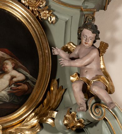 Zdjęcie nr 27: Ołtarz jednoosiowy, jednokondygnacyjny ze zwieńczeniem. Podwójny cokół z wąską, drewnianą mensą ołtarzową, wybrzuszoną. Na niej stoi tabernakulum ujęte narożnie ustawionymi spływami wolutowymi, zwieńczone spłaszczoną kopułką ze spływami wolutowymi. Retabulum flankowane dwiema ćwierć kolumnami skierowanymi po ukosie na zewnątrz, z których każda ujęta parą korynckich, kanelowanych pilastrów dźwigających przełamujące się nad nimi belkowanie i dwa faliste naczółki. Na tle pilastrów, na konsolach stoją figury św. Anny i św. Joachima oraz unoszą się na chmurach flankujące obraz uskrzydlone anioły. Zwieńczenie ujęte spływami wolutowymi, zakończone profilowanym, lekko falistym gzymsem z dwiema stykającymi się wolutami. N naczółkach dwa uskrzydlone, przepasane opaską na biodrach aniołki. W polu głównym szeroka, złocona, prostokątna rama z obrazem Matki Boskiej z Dzieciątkiem i koroną w partii belkowania, a w zwieńczeniu owalny obraz w złoconej ramie z przedstawieniem św. Józefa z Dzieciątkiem. Figury św. Anny i św. Joachima ukazane w lekkim kontrapoście, w długich, obficie fałdowanych szatach. Anna trzyma prawą rękę na piersi, w lewej przytrzymuje połę płaszcza, natomiast Joachim ręce składa w geście modlitwy. Anioły klęczą na chmurach, usytuowanych na różnych poziomach, ubrane są w miękko, ale drobno fałdowane szaty, odsłaniające ich ramiona i górną część klatki piersiowej i wskazujący na obraz. Na dekorację ornamentalną składają się drobne motywy roślinne, kampanule na ćwierćkolumnach, zwisy róż i gałązek palm wokół obrazu w zwieńczeniu i efektowna podwójna muszla palmetowa w zwieńczeniu. 