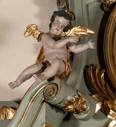 Zdjęcie nr 26: Ołtarz jednoosiowy, jednokondygnacyjny ze zwieńczeniem. Podwójny cokół z wąską, drewnianą mensą ołtarzową, wybrzuszoną. Na niej stoi tabernakulum ujęte narożnie ustawionymi spływami wolutowymi, zwieńczone spłaszczoną kopułką ze spływami wolutowymi. Retabulum flankowane dwiema ćwierć kolumnami skierowanymi po ukosie na zewnątrz, z których każda ujęta parą korynckich, kanelowanych pilastrów dźwigających przełamujące się nad nimi belkowanie i dwa faliste naczółki. Na tle pilastrów, na konsolach stoją figury św. Anny i św. Joachima oraz unoszą się na chmurach flankujące obraz uskrzydlone anioły. Zwieńczenie ujęte spływami wolutowymi, zakończone profilowanym, lekko falistym gzymsem z dwiema stykającymi się wolutami. N naczółkach dwa uskrzydlone, przepasane opaską na biodrach aniołki. W polu głównym szeroka, złocona, prostokątna rama z obrazem Matki Boskiej z Dzieciątkiem i koroną w partii belkowania, a w zwieńczeniu owalny obraz w złoconej ramie z przedstawieniem św. Józefa z Dzieciątkiem. Figury św. Anny i św. Joachima ukazane w lekkim kontrapoście, w długich, obficie fałdowanych szatach. Anna trzyma prawą rękę na piersi, w lewej przytrzymuje połę płaszcza, natomiast Joachim ręce składa w geście modlitwy. Anioły klęczą na chmurach, usytuowanych na różnych poziomach, ubrane są w miękko, ale drobno fałdowane szaty, odsłaniające ich ramiona i górną część klatki piersiowej i wskazujący na obraz. Na dekorację ornamentalną składają się drobne motywy roślinne, kampanule na ćwierćkolumnach, zwisy róż i gałązek palm wokół obrazu w zwieńczeniu i efektowna podwójna muszla palmetowa w zwieńczeniu. 