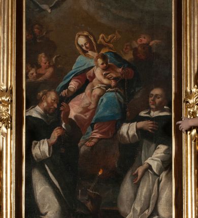 Zdjęcie nr 2: Obraz w kształcie stojącego prostokąta ukazuje siedzącą na chmurach Matkę Boską z Dzieciątkiem przekazujących różańce klęczącym pod nimi św. Dominikiem i św. Jackiem. Matka Boska ukazana jest w trzech czwartych, ubrana w różową suknię, niebieski płaszcz i brązową chustę rozwianą za plecami. W prawej ręce trzyma szkaplerz, który przekazuje św. Dominikowi. Na jej kolanach siedzi nagi Jezus, przepasany opaską na biodrach, trzymający w rękach szkaplerz zwrócony w kierunku św. Jacka. Św. Dominik ukazany z profilu, klęczący, z głową zwróconą w kierunku Marii, ubrany w dominikański habit. Klęczący św. Jacek jest zwrócony w trzech czwartych, ubrany w dominikański habit, z lewą ręką opuszczoną w dół, z prawą na piersi. W tle grupy aniołków i główek anielskich wśród chmur. 