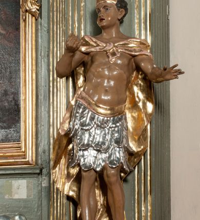 Zdjęcie nr 17: Ołtarz jednoosiowy, jednokondygnacyjny ze zwieńczeniem. Podwójny cokół z wąską, drewnianą mensą ołtarzową, wybrzuszoną. Na niej stoi tabernakulum ujęte kolumienkami i spływami wolutowymi, zwieńczone dwoma zwróconymi do siebie naczółkami z niewielką figurą baranka na tle promieni. Retabulum flankowane dwiema ćwierć kolumnami skierowanymi po ukosie na zewnątrz, z których każda ujęta parą korynckich, kanelowanych pilastrów dźwigających przełamujące się nad nimi belkowanie i dwa faliste naczółki. Na tle pilastrów, na konsolach stoją dwie figury egzotycznych mężczyzn. Zwieńczenie ujęte spływami wolutowymi, zakończone profilowanym, lekko falistym gzymsem z dwiema stykającymi się wolutami. W polu głównym szeroka, złocona, prostokątna rama z obrazem "Męczeństwo św. Bartłomieja", w zwieńczeniu owalny obraz w złoconej ramie z przedstawieniem Anioła Stróża. 
Figury egzotycznych (o typach wschodnich) mężczyzn ukazane w kontrapoście, o prawidłowych proporcjach ciała, z rękami uniesionymi przed siebie, na wysokości klatki piersiowej. Ich twarze są pełne, okrągłe o szerokich nosach i wydatnych, lekko otwartych ustach, na głowie krótkie, kręcone, ciemne włosy przytrzymane na czole złoconymi opaskami. Biodra okalają sięgające kolan spódniczki ze srebrnych piór. Mężczyzna po lewej stronie trzyma skórę z twarzą św. Bartłomieja osłaniającą część jego ciała, a postać po prawej nosi na plechach płaszcz sięgający stóp. Na dekorację ornamentalną składają się drobne motywy roślinne, kampanule na ćwierćkolumnach, kartusz ujęty drobnymi rocaille’ami, zwisy róż i gałązek palm wokół obrazu w zwieńczeniu i efektowna podwójna muszla palmetowa w zwieńczeniu. 
