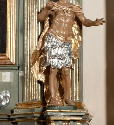 Zdjęcie nr 18: Ołtarz jednoosiowy, jednokondygnacyjny ze zwieńczeniem. Podwójny cokół z wąską, drewnianą mensą ołtarzową, wybrzuszoną. Na niej stoi tabernakulum ujęte kolumienkami i spływami wolutowymi, zwieńczone dwoma zwróconymi do siebie naczółkami z niewielką figurą baranka na tle promieni. Retabulum flankowane dwiema ćwierć kolumnami skierowanymi po ukosie na zewnątrz, z których każda ujęta parą korynckich, kanelowanych pilastrów dźwigających przełamujące się nad nimi belkowanie i dwa faliste naczółki. Na tle pilastrów, na konsolach stoją dwie figury egzotycznych mężczyzn. Zwieńczenie ujęte spływami wolutowymi, zakończone profilowanym, lekko falistym gzymsem z dwiema stykającymi się wolutami. W polu głównym szeroka, złocona, prostokątna rama z obrazem &quot;Męczeństwo św. Bartłomieja&quot;, w zwieńczeniu owalny obraz w złoconej ramie z przedstawieniem Anioła Stróża. 
Figury egzotycznych (o typach wschodnich) mężczyzn ukazane w kontrapoście, o prawidłowych proporcjach ciała, z rękami uniesionymi przed siebie, na wysokości klatki piersiowej. Ich twarze są pełne, okrągłe o szerokich nosach i wydatnych, lekko otwartych ustach, na głowie krótkie, kręcone, ciemne włosy przytrzymane na czole złoconymi opaskami. Biodra okalają sięgające kolan spódniczki ze srebrnych piór. Mężczyzna po lewej stronie trzyma skórę z twarzą św. Bartłomieja osłaniającą część jego ciała, a postać po prawej nosi na plechach płaszcz sięgający stóp. Na dekorację ornamentalną składają się drobne motywy roślinne, kampanule na ćwierćkolumnach, kartusz ujęty drobnymi rocaille’ami, zwisy róż i gałązek palm wokół obrazu w zwieńczeniu i efektowna podwójna muszla palmetowa w zwieńczeniu. 
