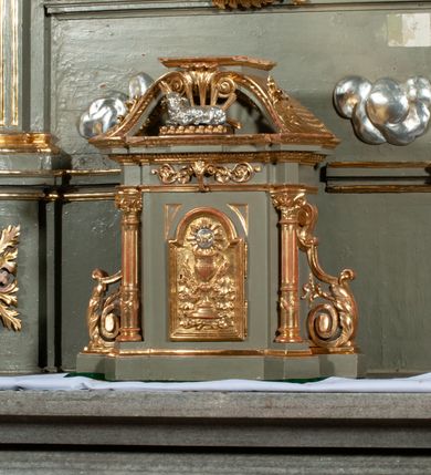 Zdjęcie nr 11: Ołtarz jednoosiowy, jednokondygnacyjny ze zwieńczeniem. Podwójny cokół z wąską, drewnianą mensą ołtarzową, wybrzuszoną. Na niej stoi tabernakulum ujęte kolumienkami i spływami wolutowymi, zwieńczone dwoma zwróconymi do siebie naczółkami z niewielką figurą baranka na tle promieni. Retabulum flankowane dwiema ćwierć kolumnami skierowanymi po ukosie na zewnątrz, z których każda ujęta parą korynckich, kanelowanych pilastrów dźwigających przełamujące się nad nimi belkowanie i dwa faliste naczółki. Na tle pilastrów, na konsolach stoją dwie figury egzotycznych mężczyzn. Zwieńczenie ujęte spływami wolutowymi, zakończone profilowanym, lekko falistym gzymsem z dwiema stykającymi się wolutami. W polu głównym szeroka, złocona, prostokątna rama z obrazem &quot;Męczeństwo św. Bartłomieja&quot;, w zwieńczeniu owalny obraz w złoconej ramie z przedstawieniem Anioła Stróża. 
Figury egzotycznych (o typach wschodnich) mężczyzn ukazane w kontrapoście, o prawidłowych proporcjach ciała, z rękami uniesionymi przed siebie, na wysokości klatki piersiowej. Ich twarze są pełne, okrągłe o szerokich nosach i wydatnych, lekko otwartych ustach, na głowie krótkie, kręcone, ciemne włosy przytrzymane na czole złoconymi opaskami. Biodra okalają sięgające kolan spódniczki ze srebrnych piór. Mężczyzna po lewej stronie trzyma skórę z twarzą św. Bartłomieja osłaniającą część jego ciała, a postać po prawej nosi na plechach płaszcz sięgający stóp. Na dekorację ornamentalną składają się drobne motywy roślinne, kampanule na ćwierćkolumnach, kartusz ujęty drobnymi rocaille’ami, zwisy róż i gałązek palm wokół obrazu w zwieńczeniu i efektowna podwójna muszla palmetowa w zwieńczeniu. 
