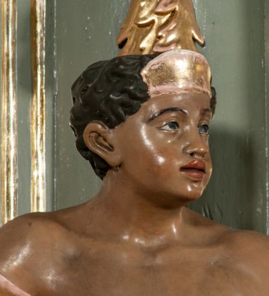 Zdjęcie nr 25: Ołtarz jednoosiowy, jednokondygnacyjny ze zwieńczeniem. Podwójny cokół z wąską, drewnianą mensą ołtarzową, wybrzuszoną. Na niej stoi tabernakulum ujęte kolumienkami i spływami wolutowymi, zwieńczone dwoma zwróconymi do siebie naczółkami z niewielką figurą baranka na tle promieni. Retabulum flankowane dwiema ćwierć kolumnami skierowanymi po ukosie na zewnątrz, z których każda ujęta parą korynckich, kanelowanych pilastrów dźwigających przełamujące się nad nimi belkowanie i dwa faliste naczółki. Na tle pilastrów, na konsolach stoją dwie figury egzotycznych mężczyzn. Zwieńczenie ujęte spływami wolutowymi, zakończone profilowanym, lekko falistym gzymsem z dwiema stykającymi się wolutami. W polu głównym szeroka, złocona, prostokątna rama z obrazem "Męczeństwo św. Bartłomieja", w zwieńczeniu owalny obraz w złoconej ramie z przedstawieniem Anioła Stróża. 
Figury egzotycznych (o typach wschodnich) mężczyzn ukazane w kontrapoście, o prawidłowych proporcjach ciała, z rękami uniesionymi przed siebie, na wysokości klatki piersiowej. Ich twarze są pełne, okrągłe o szerokich nosach i wydatnych, lekko otwartych ustach, na głowie krótkie, kręcone, ciemne włosy przytrzymane na czole złoconymi opaskami. Biodra okalają sięgające kolan spódniczki ze srebrnych piór. Mężczyzna po lewej stronie trzyma skórę z twarzą św. Bartłomieja osłaniającą część jego ciała, a postać po prawej nosi na plechach płaszcz sięgający stóp. Na dekorację ornamentalną składają się drobne motywy roślinne, kampanule na ćwierćkolumnach, kartusz ujęty drobnymi rocaille’ami, zwisy róż i gałązek palm wokół obrazu w zwieńczeniu i efektowna podwójna muszla palmetowa w zwieńczeniu. 
