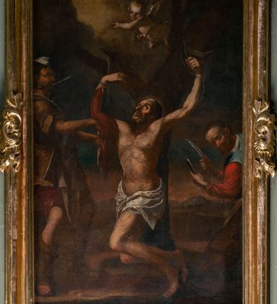 Zdjęcie nr 13: Ołtarz jednoosiowy, jednokondygnacyjny ze zwieńczeniem. Podwójny cokół z wąską, drewnianą mensą ołtarzową, wybrzuszoną. Na niej stoi tabernakulum ujęte kolumienkami i spływami wolutowymi, zwieńczone dwoma zwróconymi do siebie naczółkami z niewielką figurą baranka na tle promieni. Retabulum flankowane dwiema ćwierć kolumnami skierowanymi po ukosie na zewnątrz, z których każda ujęta parą korynckich, kanelowanych pilastrów dźwigających przełamujące się nad nimi belkowanie i dwa faliste naczółki. Na tle pilastrów, na konsolach stoją dwie figury egzotycznych mężczyzn. Zwieńczenie ujęte spływami wolutowymi, zakończone profilowanym, lekko falistym gzymsem z dwiema stykającymi się wolutami. W polu głównym szeroka, złocona, prostokątna rama z obrazem &quot;Męczeństwo św. Bartłomieja&quot;, w zwieńczeniu owalny obraz w złoconej ramie z przedstawieniem Anioła Stróża. 
Figury egzotycznych (o typach wschodnich) mężczyzn ukazane w kontrapoście, o prawidłowych proporcjach ciała, z rękami uniesionymi przed siebie, na wysokości klatki piersiowej. Ich twarze są pełne, okrągłe o szerokich nosach i wydatnych, lekko otwartych ustach, na głowie krótkie, kręcone, ciemne włosy przytrzymane na czole złoconymi opaskami. Biodra okalają sięgające kolan spódniczki ze srebrnych piór. Mężczyzna po lewej stronie trzyma skórę z twarzą św. Bartłomieja osłaniającą część jego ciała, a postać po prawej nosi na plechach płaszcz sięgający stóp. Na dekorację ornamentalną składają się drobne motywy roślinne, kampanule na ćwierćkolumnach, kartusz ujęty drobnymi rocaille’ami, zwisy róż i gałązek palm wokół obrazu w zwieńczeniu i efektowna podwójna muszla palmetowa w zwieńczeniu. 
