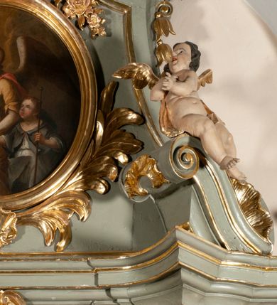 Zdjęcie nr 6: Owalny obraz ukazuje anioła prowadzącego za rękę chłopca. Anioł ukazany do kolan, w trzech czwartych, z prawą ręką uniesioną w kierunku przedstawionego na niebie oka Opatrzności i z lewą trzymającą za rękę chłopca. Jego twarz jest modelowana łagodnie, szkicowo, z otwartymi oczami, prostym nosem i drobnymi ustami oraz jasnymi włosami opadającymi na kark. Jest ubrany w żółtą suknię z trójkątnym dekoltem, krótkimi rękawami i z odsłoniętą lewą nogą oraz czerwony płaszcz przerzucony przez lewe ramię i zarzucony na plecy i prawe biodro. Za plecami widoczne są rozpostarte skrzydła. Chłopiec przedstawiony został do kolan, w trzech czwartych, w jasnej sukni i szarym płaszczu, z kijem pielgrzymim w lewej ręce. Jego twarz jest okrągła, pełna, z zaczerwionymi policzkami, oczy małe, otwarte, nos krótki, usta drobne. Tło ciemne, nieokreślone. 
