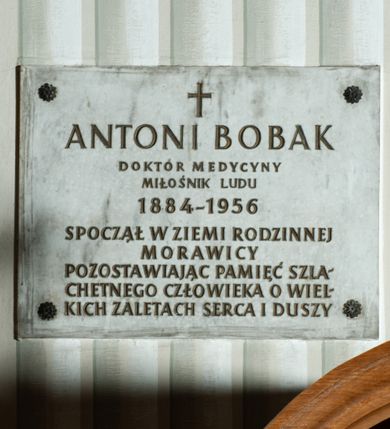Zdjęcie nr 1: Tablica w kształcie prostokąta zbliżonego do kwadratu z inskrypcją: &quot;ANTONI BOBAK / DOKTÓR MEDYCYNY / MIŁOŚNIK LUDU / 1884-1956 / SPOCZĄŁ W ZIEMI RODZINNEJ / MORAWICY / POZOSTAWIAJĄC PAMIĘCI SZLA/CHETNEGO CZŁOWIEKA O WIEL/KICH ZALETACH SERCA I DUSZY&quot;.