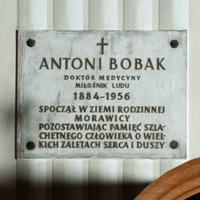 Zdjęcie nr 1: Tablica w kształcie prostokąta zbliżonego do kwadratu z inskrypcją: &quot;ANTONI BOBAK / DOKTÓR MEDYCYNY / MIŁOŚNIK LUDU / 1884-1956 / SPOCZĄŁ W ZIEMI RODZINNEJ / MORAWICY / POZOSTAWIAJĄC PAMIĘCI SZLA/CHETNEGO CZŁOWIEKA O WIEL/KICH ZALETACH SERCA I DUSZY&quot;.