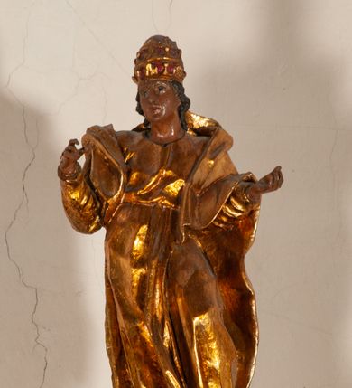 Zdjęcie nr 22: Antyambona składa się z wysokiego cokołu ujętego  szerokimi, kanelowanymi spływami wolutowymi i figurą baranka, zaplecka z obrazem ukazującym chrzest Chrystusa w Jordanie, ujętego podwieszoną kotarą i baldachim z podwieszoną pod nim kotarą. Na nim cztery esowato wygięte i łączące się górą ze sobą kabłąki, zakończone personifikacją Kościoła – kobiety w tiarze papieskiej na głowie. 