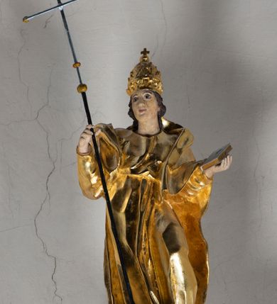 Zdjęcie nr 7: Antyambona składa się z wysokiego cokołu ujętego  szerokimi, kanelowanymi spływami wolutowymi i figurą baranka, zaplecka z obrazem ukazującym chrzest Chrystusa w Jordanie, ujętego podwieszoną kotarą i baldachim z podwieszoną pod nim kotarą. Na nim cztery esowato wygięte i łączące się górą ze sobą kabłąki, zakończone personifikacją Kościoła – kobiety w tiarze papieskiej na głowie. 