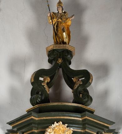 Zdjęcie nr 8: Antyambona składa się z wysokiego cokołu ujętego  szerokimi, kanelowanymi spływami wolutowymi i figurą baranka, zaplecka z obrazem ukazującym chrzest Chrystusa w Jordanie, ujętego podwieszoną kotarą i baldachim z podwieszoną pod nim kotarą. Na nim cztery esowato wygięte i łączące się górą ze sobą kabłąki, zakończone personifikacją Kościoła – kobiety w tiarze papieskiej na głowie. 