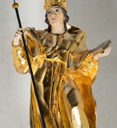 Zdjęcie nr 19: Antyambona składa się z wysokiego cokołu ujętego  szerokimi, kanelowanymi spływami wolutowymi i figurą baranka, zaplecka z obrazem ukazującym chrzest Chrystusa w Jordanie, ujętego podwieszoną kotarą i baldachim z podwieszoną pod nim kotarą. Na nim cztery esowato wygięte i łączące się górą ze sobą kabłąki, zakończone personifikacją Kościoła – kobiety w tiarze papieskiej na głowie. 