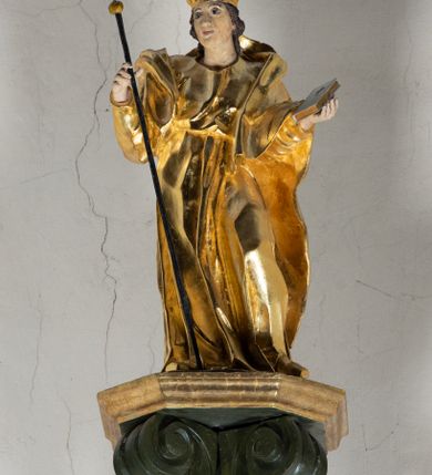 Zdjęcie nr 17: Antyambona składa się z wysokiego cokołu ujętego  szerokimi, kanelowanymi spływami wolutowymi i figurą baranka, zaplecka z obrazem ukazującym chrzest Chrystusa w Jordanie, ujętego podwieszoną kotarą i baldachim z podwieszoną pod nim kotarą. Na nim cztery esowato wygięte i łączące się górą ze sobą kabłąki, zakończone personifikacją Kościoła – kobiety w tiarze papieskiej na głowie. 