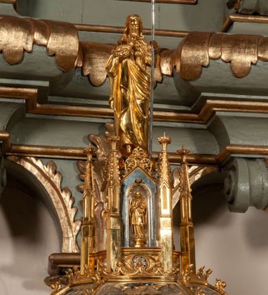 Zdjęcie nr 10: Podstawa okrągła, dwustopniowa z prostopadłościenną górną częścią, z trzonem w typie gruszkowatym z wałkiem w górnej części, podtrzymującym czarę w formie spłaszczonej kuli z puklami. Na czarze tarcza herbowa ujęta wolutami z godłem herbu Szaszor lub Orla. Pokrywa drewniana, w kształcie smukłej półkopuły o powierzchni pokrytej srebrzonymi łuskami, obwiedzionej koroną, podzielona żebrami z żabkami i zwieńczona koroną. Nad kopułą sześcioboczna wieżyczka ujęta wolnostojącymi pinaklami. Jej ścianki zakończone trójkątnie z ornamentalnymi grzebieniami, wypełnione wnękami z postaciami aniołów. Nad wieżyczką figura św. Jana Chrzciciela, ubranego w wielbłądzią skórę i płaszcz przerzucony na prawym ramieniu. W prawej dłoni podtrzymuje baranka, w lewej trzyma osadzony na długim trzpieniu krzyż. Na wewnętrznej stronie pokrywy tabliczka z inskrypcją: „CURA ET IMPENSIS / JOSEPHI PAJĄCZEWSKI / CURATI MORAVICEAEN ET / DECANI CZERNICHOVIEN A(NNO) D(OMINI) 1904 A(D) M(AIOREM) D(EI) G(LORIAM)”.        