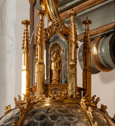 Zdjęcie nr 11: Podstawa okrągła, dwustopniowa z prostopadłościenną górną częścią, z trzonem w typie gruszkowatym z wałkiem w górnej części, podtrzymującym czarę w formie spłaszczonej kuli z puklami. Na czarze tarcza herbowa ujęta wolutami z godłem herbu Szaszor lub Orla. Pokrywa drewniana, w kształcie smukłej półkopuły o powierzchni pokrytej srebrzonymi łuskami, obwiedzionej koroną, podzielona żebrami z żabkami i zwieńczona koroną. Nad kopułą sześcioboczna wieżyczka ujęta wolnostojącymi pinaklami. Jej ścianki zakończone trójkątnie z ornamentalnymi grzebieniami, wypełnione wnękami z postaciami aniołów. Nad wieżyczką figura św. Jana Chrzciciela, ubranego w wielbłądzią skórę i płaszcz przerzucony na prawym ramieniu. W prawej dłoni podtrzymuje baranka, w lewej trzyma osadzony na długim trzpieniu krzyż. Na wewnętrznej stronie pokrywy tabliczka z inskrypcją: „CURA ET IMPENSIS / JOSEPHI PAJĄCZEWSKI / CURATI MORAVICEAEN ET / DECANI CZERNICHOVIEN A(NNO) D(OMINI) 1904 A(D) M(AIOREM) D(EI) G(LORIAM)”.        