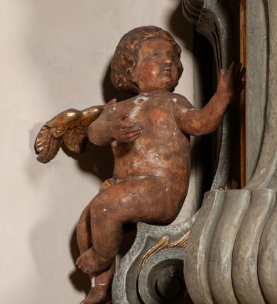 Zdjęcie nr 25: Kosz ambony na rzucie czworoboku, o bokach lekko wypukłych, wsparty na piramidalnym cokole z szyszką ujętą liśćmi. Kosz podzielony szerokimi, kanelowanymi spływami i zwieńczony gzymsem. Na ściance frontowej płaskorzeźbiona figura Chrystusa błogosławiącego trzymany w ręku bochenek chleba. Zaplecek flankowany profilowanymi listwami z kampanulami zakończonymi ulistnionymi konsolkami, pośrodku obraz w kształcie stojącego prostokąta zamkniętego łukiem półkolistym, nadwieszonym z przedstawieniem Jezusa wśród mędrców. Baldachim powielający rzut kosza, profilowany, ujęty impostami, zwieńczony czterema esowato wygiętymi i łączącymi się górą kabłąkami. Na podniebieniu baldachimu gołębica Ducha Świętego ,a tle promieni. Na nich figura Chrystusa Zmartwychwstałego, ukazanego w całej postaci, w kontrapoście, z płaszczem na plecach osłaniającym biodro. Prawą rękę unosi w geście błogosławieństwa, w lewej trzyma chorągiew. 