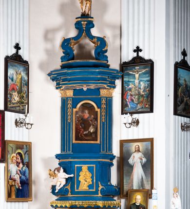 Zdjęcie nr 1: Kosz ambony na rzucie czworoboku, o bokach lekko wypukłych, wsparty na piramidalnym cokole z szyszką ujętą liśćmi. Kosz podzielony szerokimi, kanelowanymi spływami i zwieńczony gzymsem. Na ściance frontowej płaskorzeźbiona figura Chrystusa błogosławiącego trzymany w ręku bochenek chleba. Zaplecek flankowany profilowanymi listwami z kampanulami zakończonymi ulistnionymi konsolkami, pośrodku obraz w kształcie stojącego prostokąta zamkniętego łukiem półkolistym, nadwieszonym z przedstawieniem Jezusa wśród mędrców. Baldachim powielający rzut kosza, profilowany, ujęty impostami, zwieńczony czterema esowato wygiętymi i łączącymi się górą kabłąkami. Na podniebieniu baldachimu gołębica Ducha Świętego ,a tle promieni. Na nich figura Chrystusa Zmartwychwstałego, ukazanego w całej postaci, w kontrapoście, z płaszczem na plecach osłaniającym biodro. Prawą rękę unosi w geście błogosławieństwa, w lewej trzyma chorągiew. 