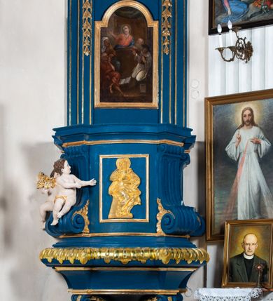 Zdjęcie nr 2: Kosz ambony na rzucie czworoboku, o bokach lekko wypukłych, wsparty na piramidalnym cokole z szyszką ujętą liśćmi. Kosz podzielony szerokimi, kanelowanymi spływami i zwieńczony gzymsem. Na ściance frontowej płaskorzeźbiona figura Chrystusa błogosławiącego trzymany w ręku bochenek chleba. Zaplecek flankowany profilowanymi listwami z kampanulami zakończonymi ulistnionymi konsolkami, pośrodku obraz w kształcie stojącego prostokąta zamkniętego łukiem półkolistym, nadwieszonym z przedstawieniem Jezusa wśród mędrców. Baldachim powielający rzut kosza, profilowany, ujęty impostami, zwieńczony czterema esowato wygiętymi i łączącymi się górą kabłąkami. Na podniebieniu baldachimu gołębica Ducha Świętego ,a tle promieni. Na nich figura Chrystusa Zmartwychwstałego, ukazanego w całej postaci, w kontrapoście, z płaszczem na plecach osłaniającym biodro. Prawą rękę unosi w geście błogosławieństwa, w lewej trzyma chorągiew. 