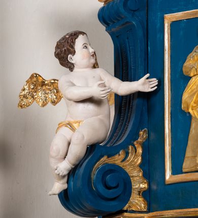 Zdjęcie nr 9: Kosz ambony na rzucie czworoboku, o bokach lekko wypukłych, wsparty na piramidalnym cokole z szyszką ujętą liśćmi. Kosz podzielony szerokimi, kanelowanymi spływami i zwieńczony gzymsem. Na ściance frontowej płaskorzeźbiona figura Chrystusa błogosławiącego trzymany w ręku bochenek chleba. Zaplecek flankowany profilowanymi listwami z kampanulami zakończonymi ulistnionymi konsolkami, pośrodku obraz w kształcie stojącego prostokąta zamkniętego łukiem półkolistym, nadwieszonym z przedstawieniem Jezusa wśród mędrców. Baldachim powielający rzut kosza, profilowany, ujęty impostami, zwieńczony czterema esowato wygiętymi i łączącymi się górą kabłąkami. Na podniebieniu baldachimu gołębica Ducha Świętego ,a tle promieni. Na nich figura Chrystusa Zmartwychwstałego, ukazanego w całej postaci, w kontrapoście, z płaszczem na plecach osłaniającym biodro. Prawą rękę unosi w geście błogosławieństwa, w lewej trzyma chorągiew. 