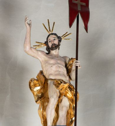 Zdjęcie nr 14: Kosz ambony na rzucie czworoboku, o bokach lekko wypukłych, wsparty na piramidalnym cokole z szyszką ujętą liśćmi. Kosz podzielony szerokimi, kanelowanymi spływami i zwieńczony gzymsem. Na ściance frontowej płaskorzeźbiona figura Chrystusa błogosławiącego trzymany w ręku bochenek chleba. Zaplecek flankowany profilowanymi listwami z kampanulami zakończonymi ulistnionymi konsolkami, pośrodku obraz w kształcie stojącego prostokąta zamkniętego łukiem półkolistym, nadwieszonym z przedstawieniem Jezusa wśród mędrców. Baldachim powielający rzut kosza, profilowany, ujęty impostami, zwieńczony czterema esowato wygiętymi i łączącymi się górą kabłąkami. Na podniebieniu baldachimu gołębica Ducha Świętego ,a tle promieni. Na nich figura Chrystusa Zmartwychwstałego, ukazanego w całej postaci, w kontrapoście, z płaszczem na plecach osłaniającym biodro. Prawą rękę unosi w geście błogosławieństwa, w lewej trzyma chorągiew. 