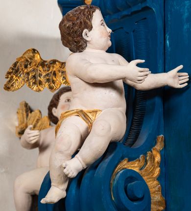 Zdjęcie nr 7: Kosz ambony na rzucie czworoboku, o bokach lekko wypukłych, wsparty na piramidalnym cokole z szyszką ujętą liśćmi. Kosz podzielony szerokimi, kanelowanymi spływami i zwieńczony gzymsem. Na ściance frontowej płaskorzeźbiona figura Chrystusa błogosławiącego trzymany w ręku bochenek chleba. Zaplecek flankowany profilowanymi listwami z kampanulami zakończonymi ulistnionymi konsolkami, pośrodku obraz w kształcie stojącego prostokąta zamkniętego łukiem półkolistym, nadwieszonym z przedstawieniem Jezusa wśród mędrców. Baldachim powielający rzut kosza, profilowany, ujęty impostami, zwieńczony czterema esowato wygiętymi i łączącymi się górą kabłąkami. Na podniebieniu baldachimu gołębica Ducha Świętego ,a tle promieni. Na nich figura Chrystusa Zmartwychwstałego, ukazanego w całej postaci, w kontrapoście, z płaszczem na plecach osłaniającym biodro. Prawą rękę unosi w geście błogosławieństwa, w lewej trzyma chorągiew. 