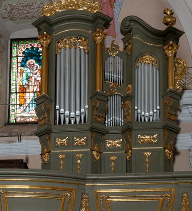 Zdjęcie nr 4: Prospekt organowy jest dwuczęściowy, czterowieżowy, zbudowany na wysokim cokole, o ośmiu rejestrach. Każda z części prospektu jest ujęta parą złoconych kolumn korynckich, stojących na ukośnie dostawionych postumentach z wolutowymi impostami. Kolumny podtrzymują spływy wolutowe zakończone wazonami płomienistymi (skrajne wieże), lub wybrzuszone łuki odcinkowe zakończone motywem rocaille'm (wewnętrzne wieże). Cztery największe rejestry przysłonięte pozłacanymi kotarami. Kontuar wolnostojący, pomiędzy obiema częściami szafy organowej, na osi założenia.