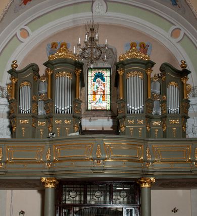 Zdjęcie nr 2: Prospekt organowy jest dwuczęściowy, czterowieżowy, zbudowany na wysokim cokole, o ośmiu rejestrach. Każda z części prospektu jest ujęta parą złoconych kolumn korynckich, stojących na ukośnie dostawionych postumentach z wolutowymi impostami. Kolumny podtrzymują spływy wolutowe zakończone wazonami płomienistymi (skrajne wieże), lub wybrzuszone łuki odcinkowe zakończone motywem rocaille'm (wewnętrzne wieże). Cztery największe rejestry przysłonięte pozłacanymi kotarami. Kontuar wolnostojący, pomiędzy obiema częściami szafy organowej, na osi założenia.