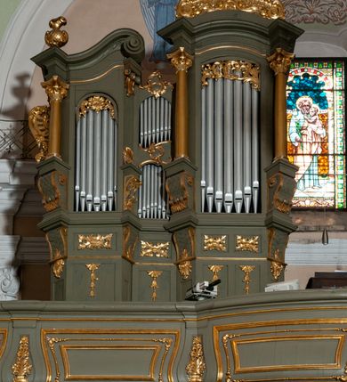 Zdjęcie nr 3: Prospekt organowy jest dwuczęściowy, czterowieżowy, zbudowany na wysokim cokole, o ośmiu rejestrach. Każda z części prospektu jest ujęta parą złoconych kolumn korynckich, stojących na ukośnie dostawionych postumentach z wolutowymi impostami. Kolumny podtrzymują spływy wolutowe zakończone wazonami płomienistymi (skrajne wieże), lub wybrzuszone łuki odcinkowe zakończone motywem rocaille'm (wewnętrzne wieże). Cztery największe rejestry przysłonięte pozłacanymi kotarami. Kontuar wolnostojący, pomiędzy obiema częściami szafy organowej, na osi założenia.