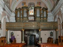 Zdjęcie nr 1: Prospekt organowy jest dwuczęściowy, czterowieżowy, zbudowany na wysokim cokole, o ośmiu rejestrach. Każda z części prospektu jest ujęta parą złoconych kolumn korynckich, stojących na ukośnie dostawionych postumentach z wolutowymi impostami. Kolumny podtrzymują spływy wolutowe zakończone wazonami płomienistymi (skrajne wieże), lub wybrzuszone łuki odcinkowe zakończone motywem rocaille&#039;m (wewnętrzne wieże). Cztery największe rejestry przysłonięte pozłacanymi kotarami. Kontuar wolnostojący, pomiędzy obiema częściami szafy organowej, na osi założenia.