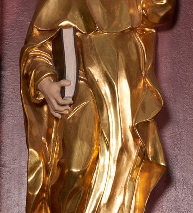Zdjęcie nr 2: Rzeźba ścięta z tyłu, zapewne wydrążona. Postać ujęta w lekkim kontrapoście, z prawą ręką trzymająca zamkniętą księgę, a w lewej trzymającą pochodnię. Jego głowa jest zwrócona w lewo i lekko uniesiona. Twarz okolona krótkim zarostem, włosy krótkie, brązowe. Święty jest ubrany w habit dominikański, mocno fałdowany w dolnej części z widocznymi brązowymi butami oraz płaszcz z kapturem. U jego stóp leży pies. Figura polichromowana naturalistycznie w partiach ciała, habit złocony, pies srebrzony, oprawa księgi pomalowana na kolor brązowy. 