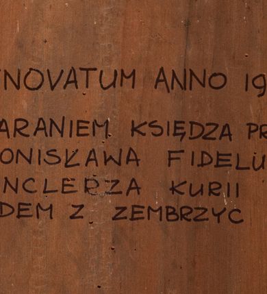 Zdjęcie nr 4: Obraz w kształcie stojącego prostokąta przedstawiający Matkę Boską Szkaplerzną z Dzieciątkiem i świętymi karmelitańskimi. W centrum kompozycji tronująca Matka Boska z Dzieciątkiem na kolanach, po bokach której klęczą św. Szymon Stock i św. Teresa z Avilli. Matka Boska ukazana jest frontalnie z głową pochyloną delikatnie w prawo, prawą ręką opuszczoną wzdłuż ciała i podaje szkaplerz św. Szymonowi, a lewą podtrzymuje Dzieciątko. Twarz Marii owalna o delikatnych rysach z długim i wąskim nosem oraz drobnymi ustami, głowa okolona ciemnobrązowymi, długimi włosami z przedziałkiem na środku. Ubrana jest w czerwoną suknię z białym kołnierzykiem u szyi oraz niebieski płaszcz z ciemnozieloną podszewką z jedną połą ułożoną na kolanach. Głowa ujęta nimbem, a na niej założony biały welon i otwarta korona. Dzieciątko zwrócone trzy czwarte w lewo, w postawie stojącej, rączkami przekazuje szkaplerz św. Teresie. Twarz Dzieciątka okrągła z wąskim nosem, małymi ustami i silnie zarumienionymi policzkami. Głowa okolona jasnymi i krótkimi włosami, wokół niej promienisty nimb. Ubrane jest w białą tkaninę, przewiązaną w biodrach. Po lewej stronie obrazu klęczy św. Szymon Stock ukazany z prawego profilu rękami sięgający po szkaplerz. Twarz szczupła o śniadej karnacji, okolona zarostem, prosty nos, głęboko osadzone oczy patrzące w górę; na głowie tonsura. Święty ubrany jest w brązowy habit oraz biały karmelitański płaszcz. Za nim ustawieni są czterej członkowie bractwa w czarnych kapach brackich. Święta Teresa zwrócona jest w trzech czwartych w prawo, ukazana w pozycji klęczącej, prawą ręką odbiera szkaplerz z rąk Dzieciątka, a w lewej trzyma różaniec. Twarz owalna o ciemnobrązowych oczach uniesionych ku górze, prostym nosie i wydatnym podbródku. Święta ubrana jest w habit i płaszcz karmelitański z podwiką i welonem. Za nią stoją dwie kobiety. Po bokach Marii i Dzieciątka są skłębione chmury i po trzy uskrzydlone główki anielskie z każdej strony. Tło w dolnej części ciemne i pochmurne, w górnej złote. Na odwrociu napis: „RENOVATUM ANNO 1990 / STARANIEM KSIĘDZA PRAŁATA / BRONISŁAWA FIDELUSA / KANCLERZA KURII / RODEM Z ZEMBRZYC”.