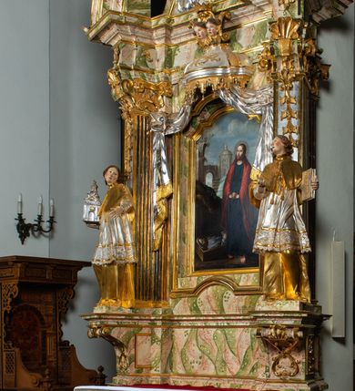 Zdjęcie nr 13: Ołtarz drewniany, prostopadłościenny z kamienną mensą, z kamiennym portatylem. Antepedium drewniane ujęte marmoryzowaną ramą z karbowanym profilem. W polu owalny medalion z przedstawieniem świętego z zakonu Marków, ujętym wicią akantową przeplatana z kwiatową. Nastawa ołtarzowa architektoniczna, jednoosiowa, jednokondygnacyjna ze zwieńczeniem na cokole.  Retabulum flankowane parą zdwojonych półfilarów zakończonych konsolami,  dźwigających pełne belkowanie oraz fragmenty przerwanego, półkolistego przyczółka z siedzącymi puttami. Na tle pilastrów, na konsolach ustawione figury dwóch świętych. Trzony pilastrów dekorowane kampanulami. W polu środkowym wnęka w formie stojącego prostokąta zamkniętego łukiem segmentowym nadwieszonego z uskokiem ujęta profilowaną ramą, z obrazem Wskrzeszenie Łazarza, w osobnej ramie. Nad wnęką baldachim dekorowany lambrekinem, z podwieszoną tkaniną po dwóch stronach, lamowaną frędzlą. Nam baldachimem kartusz z uskrzydlonymi główkami anielskimi i zwieńczony koroną. Zwieńczenie w formie zbliżonej do trapezu o wklęsłych bokach zamknięte falistym gzymsem, dekorowanym kampanulami. W polu gorejące serce przebite mieczem, w otoku z obłoków i uskrzydlonych główek anielskich, w glorii promienistej.  Struktura polichromowana w sposób imitujący marmoryzację w kolorze beżowo-zielonym. Ornamentyka i profile złocone, detal i zwieńczenie srebrzone.