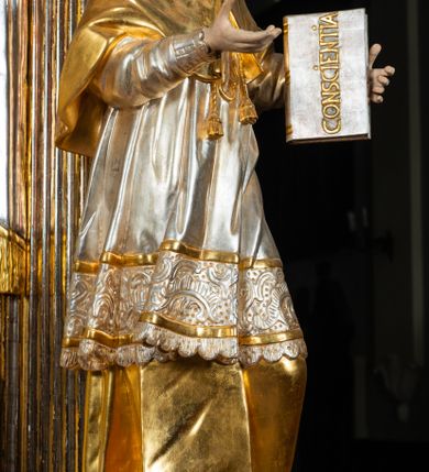 Zdjęcie nr 65: Ołtarz drewniany, prostopadłościenny z kamienną mensą, z kamiennym portatylem. Antepedium drewniane ujęte marmoryzowaną ramą z karbowanym profilem. W polu owalny medalion z przedstawieniem świętego z zakonu Marków, ujętym wicią akantową przeplatana z kwiatową. Nastawa ołtarzowa architektoniczna, jednoosiowa, jednokondygnacyjna ze zwieńczeniem na cokole.  Retabulum flankowane parą zdwojonych półfilarów zakończonych konsolami,  dźwigających pełne belkowanie oraz fragmenty przerwanego, półkolistego przyczółka z siedzącymi puttami. Na tle pilastrów, na konsolach ustawione figury dwóch świętych. Trzony pilastrów dekorowane kampanulami. W polu środkowym wnęka w formie stojącego prostokąta zamkniętego łukiem segmentowym nadwieszonego z uskokiem ujęta profilowaną ramą, z obrazem Wskrzeszenie Łazarza, w osobnej ramie. Nad wnęką baldachim dekorowany lambrekinem, z podwieszoną tkaniną po dwóch stronach, lamowaną frędzlą. Nam baldachimem kartusz z uskrzydlonymi główkami anielskimi i zwieńczony koroną. Zwieńczenie w formie zbliżonej do trapezu o wklęsłych bokach zamknięte falistym gzymsem, dekorowanym kampanulami. W polu gorejące serce przebite mieczem, w otoku z obłoków i uskrzydlonych główek anielskich, w glorii promienistej.  Struktura polichromowana w sposób imitujący marmoryzację w kolorze beżowo-zielonym. Ornamentyka i profile złocone, detal i zwieńczenie srebrzone.