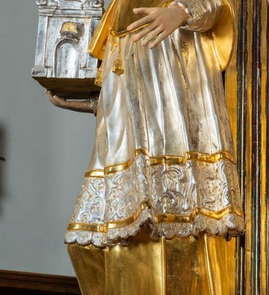 Zdjęcie nr 4: Ołtarz drewniany, prostopadłościenny z kamienną mensą, z kamiennym portatylem. Antepedium drewniane ujęte marmoryzowaną ramą z karbowanym profilem. W polu owalny medalion z przedstawieniem świętego z zakonu Marków, ujętym wicią akantową przeplatana z kwiatową. Nastawa ołtarzowa architektoniczna, jednoosiowa, jednokondygnacyjna ze zwieńczeniem na cokole.  Retabulum flankowane parą zdwojonych półfilarów zakończonych konsolami,  dźwigających pełne belkowanie oraz fragmenty przerwanego, półkolistego przyczółka z siedzącymi puttami. Na tle pilastrów, na konsolach ustawione figury dwóch świętych. Trzony pilastrów dekorowane kampanulami. W polu środkowym wnęka w formie stojącego prostokąta zamkniętego łukiem segmentowym nadwieszonego z uskokiem ujęta profilowaną ramą, z obrazem Wskrzeszenie Łazarza, w osobnej ramie. Nad wnęką baldachim dekorowany lambrekinem, z podwieszoną tkaniną po dwóch stronach, lamowaną frędzlą. Nam baldachimem kartusz z uskrzydlonymi główkami anielskimi i zwieńczony koroną. Zwieńczenie w formie zbliżonej do trapezu o wklęsłych bokach zamknięte falistym gzymsem, dekorowanym kampanulami. W polu gorejące serce przebite mieczem, w otoku z obłoków i uskrzydlonych główek anielskich, w glorii promienistej.  Struktura polichromowana w sposób imitujący marmoryzację w kolorze beżowo-zielonym. Ornamentyka i profile złocone, detal i zwieńczenie srebrzone.