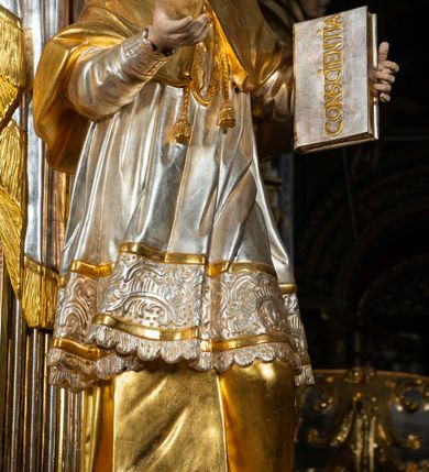 Zdjęcie nr 8: Ołtarz drewniany, prostopadłościenny z kamienną mensą, z kamiennym portatylem. Antepedium drewniane ujęte marmoryzowaną ramą z karbowanym profilem. W polu owalny medalion z przedstawieniem świętego z zakonu Marków, ujętym wicią akantową przeplatana z kwiatową. Nastawa ołtarzowa architektoniczna, jednoosiowa, jednokondygnacyjna ze zwieńczeniem na cokole.  Retabulum flankowane parą zdwojonych półfilarów zakończonych konsolami,  dźwigających pełne belkowanie oraz fragmenty przerwanego, półkolistego przyczółka z siedzącymi puttami. Na tle pilastrów, na konsolach ustawione figury dwóch świętych. Trzony pilastrów dekorowane kampanulami. W polu środkowym wnęka w formie stojącego prostokąta zamkniętego łukiem segmentowym nadwieszonego z uskokiem ujęta profilowaną ramą, z obrazem Wskrzeszenie Łazarza, w osobnej ramie. Nad wnęką baldachim dekorowany lambrekinem, z podwieszoną tkaniną po dwóch stronach, lamowaną frędzlą. Nam baldachimem kartusz z uskrzydlonymi główkami anielskimi i zwieńczony koroną. Zwieńczenie w formie zbliżonej do trapezu o wklęsłych bokach zamknięte falistym gzymsem, dekorowanym kampanulami. W polu gorejące serce przebite mieczem, w otoku z obłoków i uskrzydlonych główek anielskich, w glorii promienistej.  Struktura polichromowana w sposób imitujący marmoryzację w kolorze beżowo-zielonym. Ornamentyka i profile złocone, detal i zwieńczenie srebrzone.