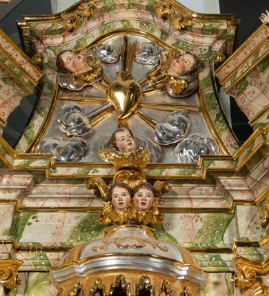 Zdjęcie nr 46: Ołtarz drewniany, prostopadłościenny z kamienną mensą, z kamiennym portatylem. Antepedium drewniane ujęte marmoryzowaną ramą z karbowanym profilem. W polu owalny medalion z przedstawieniem świętego z zakonu Marków, ujętym wicią akantową przeplatana z kwiatową. Nastawa ołtarzowa architektoniczna, jednoosiowa, jednokondygnacyjna ze zwieńczeniem na cokole.  Retabulum flankowane parą zdwojonych półfilarów zakończonych konsolami,  dźwigających pełne belkowanie oraz fragmenty przerwanego, półkolistego przyczółka z siedzącymi puttami. Na tle pilastrów, na konsolach ustawione figury dwóch świętych. Trzony pilastrów dekorowane kampanulami. W polu środkowym wnęka w formie stojącego prostokąta zamkniętego łukiem segmentowym nadwieszonego z uskokiem ujęta profilowaną ramą, z obrazem Wskrzeszenie Łazarza, w osobnej ramie. Nad wnęką baldachim dekorowany lambrekinem, z podwieszoną tkaniną po dwóch stronach, lamowaną frędzlą. Nam baldachimem kartusz z uskrzydlonymi główkami anielskimi i zwieńczony koroną. Zwieńczenie w formie zbliżonej do trapezu o wklęsłych bokach zamknięte falistym gzymsem, dekorowanym kampanulami. W polu gorejące serce przebite mieczem, w otoku z obłoków i uskrzydlonych główek anielskich, w glorii promienistej.  Struktura polichromowana w sposób imitujący marmoryzację w kolorze beżowo-zielonym. Ornamentyka i profile złocone, detal i zwieńczenie srebrzone.