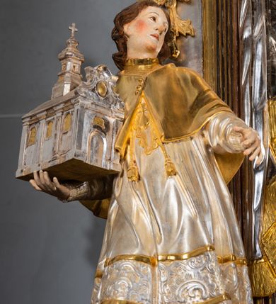 Zdjęcie nr 21: Ołtarz drewniany, prostopadłościenny z kamienną mensą, z kamiennym portatylem. Antepedium drewniane ujęte marmoryzowaną ramą z karbowanym profilem. W polu owalny medalion z przedstawieniem świętego z zakonu Marków, ujętym wicią akantową przeplatana z kwiatową. Nastawa ołtarzowa architektoniczna, jednoosiowa, jednokondygnacyjna ze zwieńczeniem na cokole.  Retabulum flankowane parą zdwojonych półfilarów zakończonych konsolami,  dźwigających pełne belkowanie oraz fragmenty przerwanego, półkolistego przyczółka z siedzącymi puttami. Na tle pilastrów, na konsolach ustawione figury dwóch świętych. Trzony pilastrów dekorowane kampanulami. W polu środkowym wnęka w formie stojącego prostokąta zamkniętego łukiem segmentowym nadwieszonego z uskokiem ujęta profilowaną ramą, z obrazem Wskrzeszenie Łazarza, w osobnej ramie. Nad wnęką baldachim dekorowany lambrekinem, z podwieszoną tkaniną po dwóch stronach, lamowaną frędzlą. Nam baldachimem kartusz z uskrzydlonymi główkami anielskimi i zwieńczony koroną. Zwieńczenie w formie zbliżonej do trapezu o wklęsłych bokach zamknięte falistym gzymsem, dekorowanym kampanulami. W polu gorejące serce przebite mieczem, w otoku z obłoków i uskrzydlonych główek anielskich, w glorii promienistej.  Struktura polichromowana w sposób imitujący marmoryzację w kolorze beżowo-zielonym. Ornamentyka i profile złocone, detal i zwieńczenie srebrzone.