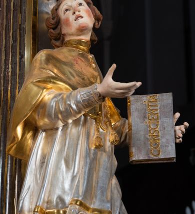 Zdjęcie nr 22: Ołtarz drewniany, prostopadłościenny z kamienną mensą, z kamiennym portatylem. Antepedium drewniane ujęte marmoryzowaną ramą z karbowanym profilem. W polu owalny medalion z przedstawieniem świętego z zakonu Marków, ujętym wicią akantową przeplatana z kwiatową. Nastawa ołtarzowa architektoniczna, jednoosiowa, jednokondygnacyjna ze zwieńczeniem na cokole.  Retabulum flankowane parą zdwojonych półfilarów zakończonych konsolami,  dźwigających pełne belkowanie oraz fragmenty przerwanego, półkolistego przyczółka z siedzącymi puttami. Na tle pilastrów, na konsolach ustawione figury dwóch świętych. Trzony pilastrów dekorowane kampanulami. W polu środkowym wnęka w formie stojącego prostokąta zamkniętego łukiem segmentowym nadwieszonego z uskokiem ujęta profilowaną ramą, z obrazem Wskrzeszenie Łazarza, w osobnej ramie. Nad wnęką baldachim dekorowany lambrekinem, z podwieszoną tkaniną po dwóch stronach, lamowaną frędzlą. Nam baldachimem kartusz z uskrzydlonymi główkami anielskimi i zwieńczony koroną. Zwieńczenie w formie zbliżonej do trapezu o wklęsłych bokach zamknięte falistym gzymsem, dekorowanym kampanulami. W polu gorejące serce przebite mieczem, w otoku z obłoków i uskrzydlonych główek anielskich, w glorii promienistej.  Struktura polichromowana w sposób imitujący marmoryzację w kolorze beżowo-zielonym. Ornamentyka i profile złocone, detal i zwieńczenie srebrzone.