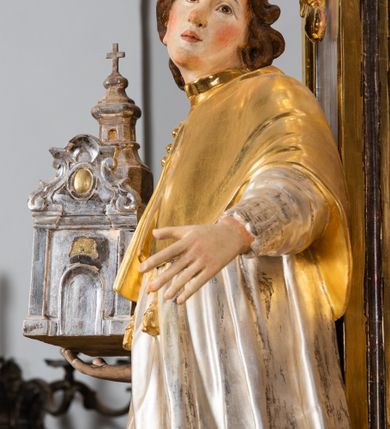 Zdjęcie nr 26: Ołtarz drewniany, prostopadłościenny z kamienną mensą, z kamiennym portatylem. Antepedium drewniane ujęte marmoryzowaną ramą z karbowanym profilem. W polu owalny medalion z przedstawieniem świętego z zakonu Marków, ujętym wicią akantową przeplatana z kwiatową. Nastawa ołtarzowa architektoniczna, jednoosiowa, jednokondygnacyjna ze zwieńczeniem na cokole.  Retabulum flankowane parą zdwojonych półfilarów zakończonych konsolami,  dźwigających pełne belkowanie oraz fragmenty przerwanego, półkolistego przyczółka z siedzącymi puttami. Na tle pilastrów, na konsolach ustawione figury dwóch świętych. Trzony pilastrów dekorowane kampanulami. W polu środkowym wnęka w formie stojącego prostokąta zamkniętego łukiem segmentowym nadwieszonego z uskokiem ujęta profilowaną ramą, z obrazem Wskrzeszenie Łazarza, w osobnej ramie. Nad wnęką baldachim dekorowany lambrekinem, z podwieszoną tkaniną po dwóch stronach, lamowaną frędzlą. Nam baldachimem kartusz z uskrzydlonymi główkami anielskimi i zwieńczony koroną. Zwieńczenie w formie zbliżonej do trapezu o wklęsłych bokach zamknięte falistym gzymsem, dekorowanym kampanulami. W polu gorejące serce przebite mieczem, w otoku z obłoków i uskrzydlonych główek anielskich, w glorii promienistej.  Struktura polichromowana w sposób imitujący marmoryzację w kolorze beżowo-zielonym. Ornamentyka i profile złocone, detal i zwieńczenie srebrzone.