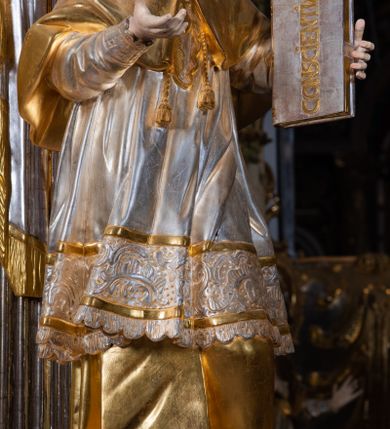 Zdjęcie nr 36: Ołtarz drewniany, prostopadłościenny z kamienną mensą, z kamiennym portatylem. Antepedium drewniane ujęte marmoryzowaną ramą z karbowanym profilem. W polu owalny medalion z przedstawieniem świętego z zakonu Marków, ujętym wicią akantową przeplatana z kwiatową. Nastawa ołtarzowa architektoniczna, jednoosiowa, jednokondygnacyjna ze zwieńczeniem na cokole.  Retabulum flankowane parą zdwojonych półfilarów zakończonych konsolami,  dźwigających pełne belkowanie oraz fragmenty przerwanego, półkolistego przyczółka z siedzącymi puttami. Na tle pilastrów, na konsolach ustawione figury dwóch świętych. Trzony pilastrów dekorowane kampanulami. W polu środkowym wnęka w formie stojącego prostokąta zamkniętego łukiem segmentowym nadwieszonego z uskokiem ujęta profilowaną ramą, z obrazem Wskrzeszenie Łazarza, w osobnej ramie. Nad wnęką baldachim dekorowany lambrekinem, z podwieszoną tkaniną po dwóch stronach, lamowaną frędzlą. Nam baldachimem kartusz z uskrzydlonymi główkami anielskimi i zwieńczony koroną. Zwieńczenie w formie zbliżonej do trapezu o wklęsłych bokach zamknięte falistym gzymsem, dekorowanym kampanulami. W polu gorejące serce przebite mieczem, w otoku z obłoków i uskrzydlonych główek anielskich, w glorii promienistej.  Struktura polichromowana w sposób imitujący marmoryzację w kolorze beżowo-zielonym. Ornamentyka i profile złocone, detal i zwieńczenie srebrzone.