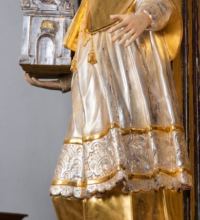 Zdjęcie nr 33: Ołtarz drewniany, prostopadłościenny z kamienną mensą, z kamiennym portatylem. Antepedium drewniane ujęte marmoryzowaną ramą z karbowanym profilem. W polu owalny medalion z przedstawieniem świętego z zakonu Marków, ujętym wicią akantową przeplatana z kwiatową. Nastawa ołtarzowa architektoniczna, jednoosiowa, jednokondygnacyjna ze zwieńczeniem na cokole.  Retabulum flankowane parą zdwojonych półfilarów zakończonych konsolami,  dźwigających pełne belkowanie oraz fragmenty przerwanego, półkolistego przyczółka z siedzącymi puttami. Na tle pilastrów, na konsolach ustawione figury dwóch świętych. Trzony pilastrów dekorowane kampanulami. W polu środkowym wnęka w formie stojącego prostokąta zamkniętego łukiem segmentowym nadwieszonego z uskokiem ujęta profilowaną ramą, z obrazem Wskrzeszenie Łazarza, w osobnej ramie. Nad wnęką baldachim dekorowany lambrekinem, z podwieszoną tkaniną po dwóch stronach, lamowaną frędzlą. Nam baldachimem kartusz z uskrzydlonymi główkami anielskimi i zwieńczony koroną. Zwieńczenie w formie zbliżonej do trapezu o wklęsłych bokach zamknięte falistym gzymsem, dekorowanym kampanulami. W polu gorejące serce przebite mieczem, w otoku z obłoków i uskrzydlonych główek anielskich, w glorii promienistej.  Struktura polichromowana w sposób imitujący marmoryzację w kolorze beżowo-zielonym. Ornamentyka i profile złocone, detal i zwieńczenie srebrzone.