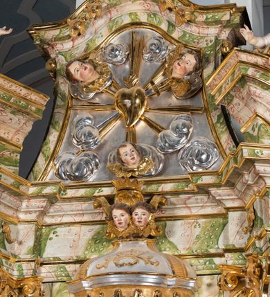 Zdjęcie nr 41: Ołtarz drewniany, prostopadłościenny z kamienną mensą, z kamiennym portatylem. Antepedium drewniane ujęte marmoryzowaną ramą z karbowanym profilem. W polu owalny medalion z przedstawieniem świętego z zakonu Marków, ujętym wicią akantową przeplatana z kwiatową. Nastawa ołtarzowa architektoniczna, jednoosiowa, jednokondygnacyjna ze zwieńczeniem na cokole.  Retabulum flankowane parą zdwojonych półfilarów zakończonych konsolami,  dźwigających pełne belkowanie oraz fragmenty przerwanego, półkolistego przyczółka z siedzącymi puttami. Na tle pilastrów, na konsolach ustawione figury dwóch świętych. Trzony pilastrów dekorowane kampanulami. W polu środkowym wnęka w formie stojącego prostokąta zamkniętego łukiem segmentowym nadwieszonego z uskokiem ujęta profilowaną ramą, z obrazem Wskrzeszenie Łazarza, w osobnej ramie. Nad wnęką baldachim dekorowany lambrekinem, z podwieszoną tkaniną po dwóch stronach, lamowaną frędzlą. Nam baldachimem kartusz z uskrzydlonymi główkami anielskimi i zwieńczony koroną. Zwieńczenie w formie zbliżonej do trapezu o wklęsłych bokach zamknięte falistym gzymsem, dekorowanym kampanulami. W polu gorejące serce przebite mieczem, w otoku z obłoków i uskrzydlonych główek anielskich, w glorii promienistej.  Struktura polichromowana w sposób imitujący marmoryzację w kolorze beżowo-zielonym. Ornamentyka i profile złocone, detal i zwieńczenie srebrzone.