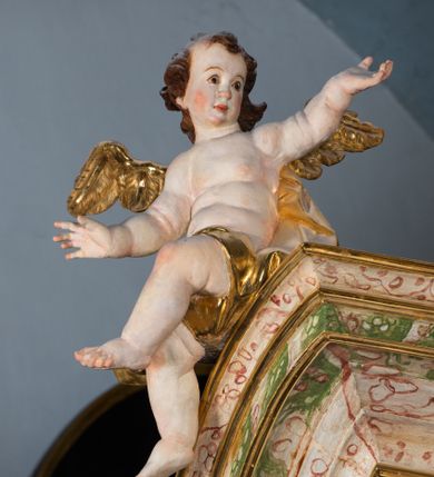 Zdjęcie nr 38: Ołtarz drewniany, prostopadłościenny z kamienną mensą, z kamiennym portatylem. Antepedium drewniane ujęte marmoryzowaną ramą z karbowanym profilem. W polu owalny medalion z przedstawieniem świętego z zakonu Marków, ujętym wicią akantową przeplatana z kwiatową. Nastawa ołtarzowa architektoniczna, jednoosiowa, jednokondygnacyjna ze zwieńczeniem na cokole.  Retabulum flankowane parą zdwojonych półfilarów zakończonych konsolami,  dźwigających pełne belkowanie oraz fragmenty przerwanego, półkolistego przyczółka z siedzącymi puttami. Na tle pilastrów, na konsolach ustawione figury dwóch świętych. Trzony pilastrów dekorowane kampanulami. W polu środkowym wnęka w formie stojącego prostokąta zamkniętego łukiem segmentowym nadwieszonego z uskokiem ujęta profilowaną ramą, z obrazem Wskrzeszenie Łazarza, w osobnej ramie. Nad wnęką baldachim dekorowany lambrekinem, z podwieszoną tkaniną po dwóch stronach, lamowaną frędzlą. Nam baldachimem kartusz z uskrzydlonymi główkami anielskimi i zwieńczony koroną. Zwieńczenie w formie zbliżonej do trapezu o wklęsłych bokach zamknięte falistym gzymsem, dekorowanym kampanulami. W polu gorejące serce przebite mieczem, w otoku z obłoków i uskrzydlonych główek anielskich, w glorii promienistej.  Struktura polichromowana w sposób imitujący marmoryzację w kolorze beżowo-zielonym. Ornamentyka i profile złocone, detal i zwieńczenie srebrzone.