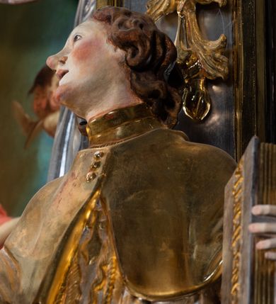 Zdjęcie nr 44: Ołtarz drewniany, prostopadłościenny z kamienną mensą, z kamiennym portatylem. Antepedium drewniane ujęte marmoryzowaną ramą z karbowanym profilem. W polu owalny medalion z przedstawieniem świętego z zakonu Marków, ujętym wicią akantową przeplatana z kwiatową. Nastawa ołtarzowa architektoniczna, jednoosiowa, jednokondygnacyjna ze zwieńczeniem na cokole.  Retabulum flankowane parą zdwojonych półfilarów zakończonych konsolami,  dźwigających pełne belkowanie oraz fragmenty przerwanego, półkolistego przyczółka z siedzącymi puttami. Na tle pilastrów, na konsolach ustawione figury dwóch świętych. Trzony pilastrów dekorowane kampanulami. W polu środkowym wnęka w formie stojącego prostokąta zamkniętego łukiem segmentowym nadwieszonego z uskokiem ujęta profilowaną ramą, z obrazem Wskrzeszenie Łazarza, w osobnej ramie. Nad wnęką baldachim dekorowany lambrekinem, z podwieszoną tkaniną po dwóch stronach, lamowaną frędzlą. Nam baldachimem kartusz z uskrzydlonymi główkami anielskimi i zwieńczony koroną. Zwieńczenie w formie zbliżonej do trapezu o wklęsłych bokach zamknięte falistym gzymsem, dekorowanym kampanulami. W polu gorejące serce przebite mieczem, w otoku z obłoków i uskrzydlonych główek anielskich, w glorii promienistej.  Struktura polichromowana w sposób imitujący marmoryzację w kolorze beżowo-zielonym. Ornamentyka i profile złocone, detal i zwieńczenie srebrzone.