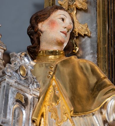 Zdjęcie nr 45: Ołtarz drewniany, prostopadłościenny z kamienną mensą, z kamiennym portatylem. Antepedium drewniane ujęte marmoryzowaną ramą z karbowanym profilem. W polu owalny medalion z przedstawieniem świętego z zakonu Marków, ujętym wicią akantową przeplatana z kwiatową. Nastawa ołtarzowa architektoniczna, jednoosiowa, jednokondygnacyjna ze zwieńczeniem na cokole.  Retabulum flankowane parą zdwojonych półfilarów zakończonych konsolami,  dźwigających pełne belkowanie oraz fragmenty przerwanego, półkolistego przyczółka z siedzącymi puttami. Na tle pilastrów, na konsolach ustawione figury dwóch świętych. Trzony pilastrów dekorowane kampanulami. W polu środkowym wnęka w formie stojącego prostokąta zamkniętego łukiem segmentowym nadwieszonego z uskokiem ujęta profilowaną ramą, z obrazem Wskrzeszenie Łazarza, w osobnej ramie. Nad wnęką baldachim dekorowany lambrekinem, z podwieszoną tkaniną po dwóch stronach, lamowaną frędzlą. Nam baldachimem kartusz z uskrzydlonymi główkami anielskimi i zwieńczony koroną. Zwieńczenie w formie zbliżonej do trapezu o wklęsłych bokach zamknięte falistym gzymsem, dekorowanym kampanulami. W polu gorejące serce przebite mieczem, w otoku z obłoków i uskrzydlonych główek anielskich, w glorii promienistej.  Struktura polichromowana w sposób imitujący marmoryzację w kolorze beżowo-zielonym. Ornamentyka i profile złocone, detal i zwieńczenie srebrzone.