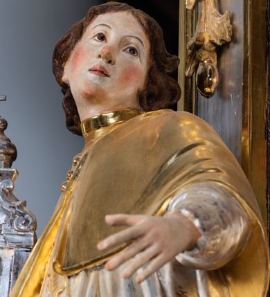 Zdjęcie nr 50: Ołtarz drewniany, prostopadłościenny z kamienną mensą, z kamiennym portatylem. Antepedium drewniane ujęte marmoryzowaną ramą z karbowanym profilem. W polu owalny medalion z przedstawieniem świętego z zakonu Marków, ujętym wicią akantową przeplatana z kwiatową. Nastawa ołtarzowa architektoniczna, jednoosiowa, jednokondygnacyjna ze zwieńczeniem na cokole.  Retabulum flankowane parą zdwojonych półfilarów zakończonych konsolami,  dźwigających pełne belkowanie oraz fragmenty przerwanego, półkolistego przyczółka z siedzącymi puttami. Na tle pilastrów, na konsolach ustawione figury dwóch świętych. Trzony pilastrów dekorowane kampanulami. W polu środkowym wnęka w formie stojącego prostokąta zamkniętego łukiem segmentowym nadwieszonego z uskokiem ujęta profilowaną ramą, z obrazem Wskrzeszenie Łazarza, w osobnej ramie. Nad wnęką baldachim dekorowany lambrekinem, z podwieszoną tkaniną po dwóch stronach, lamowaną frędzlą. Nam baldachimem kartusz z uskrzydlonymi główkami anielskimi i zwieńczony koroną. Zwieńczenie w formie zbliżonej do trapezu o wklęsłych bokach zamknięte falistym gzymsem, dekorowanym kampanulami. W polu gorejące serce przebite mieczem, w otoku z obłoków i uskrzydlonych główek anielskich, w glorii promienistej.  Struktura polichromowana w sposób imitujący marmoryzację w kolorze beżowo-zielonym. Ornamentyka i profile złocone, detal i zwieńczenie srebrzone.